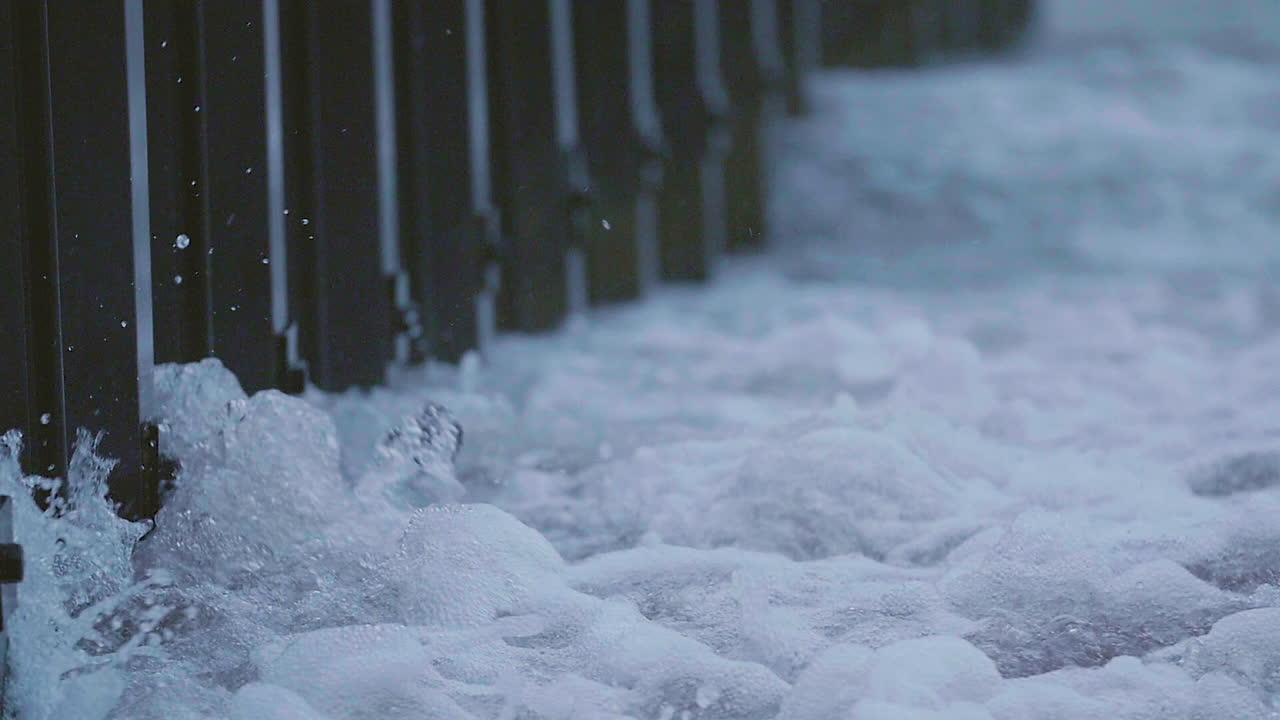 Waves crash along the metal sea wall of the Great Lakes. Rain falls during the grey day on the edge of the midwest.