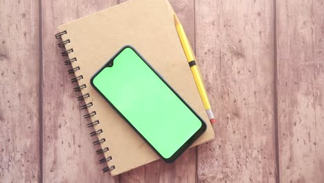 smartphone on notebook with green screen and pencil