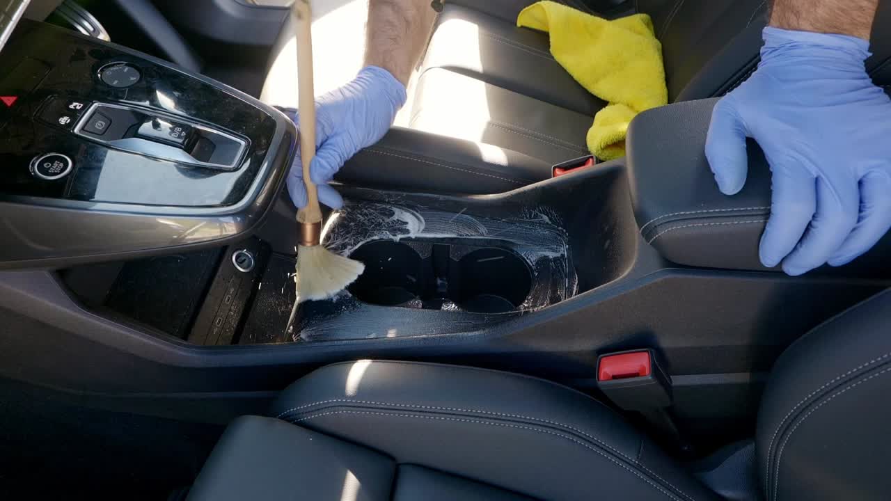 Cleaning car cup holders and centre console with large brush with wooden handle - wide shot