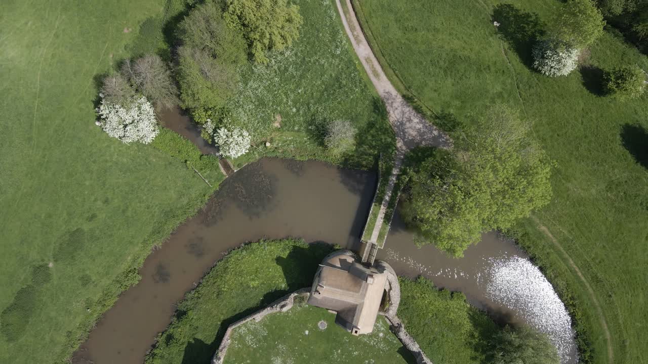 Aerial view of Stogursey Castle, a medieval castle in Somerset, England. Most of the site is in ruins, with a thatched gatehouse used for holiday's. Drone moving forward over the ruins and moat. 4K