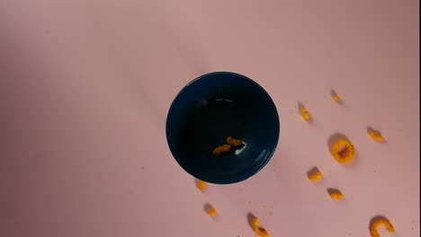 Top-view-clip-of-cheese-rings-falling-and-scattering-around-a-blue-ceramic-bowl