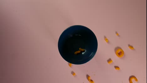clip de vista superior de anillos de queso cayendo y esparciéndose alrededor de un cuenco de cerámica azul