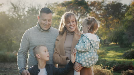 portrait of a young healthy family - a couple with two children. smiling, looking at the camera. standing in the autumn park