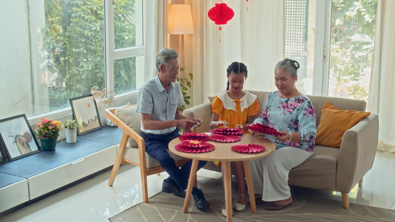 Grandparents and Girl Crafting New Year Decorations at Round Table