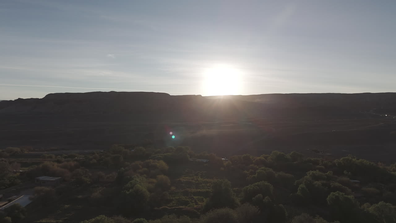 Forwards flying drone shot above San Pedro de Atacama Chile South America on a blue but cloudy day with mountains in the background and the sun setting behind LOG