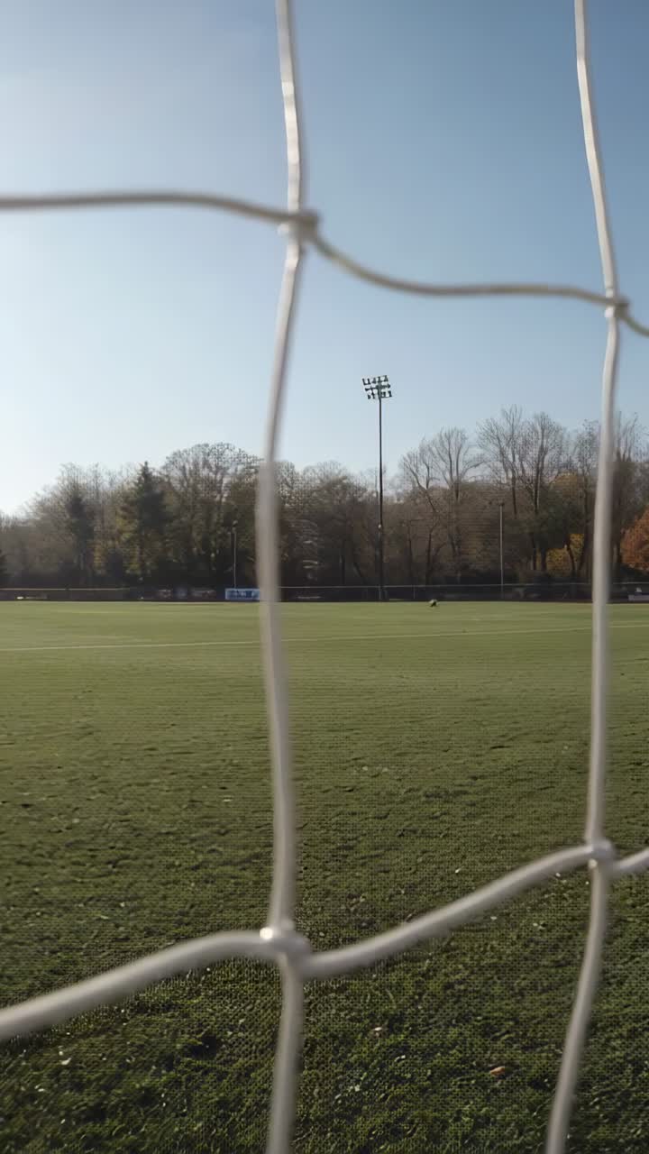 Camera nudging behind soccer goal net, causing net sway and revealing field for sports framing