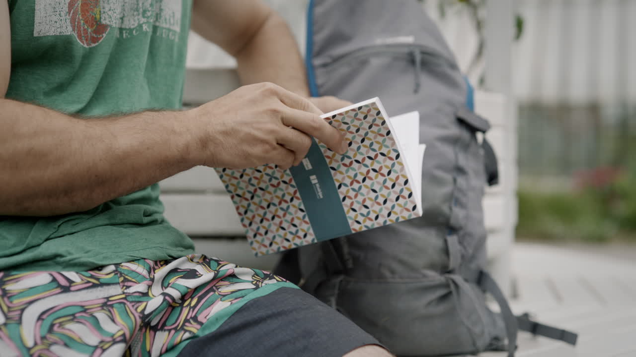 공원에 배낭을 메고 벤치에 앉아 하이킹에 관한 소책자를 읽는 남자