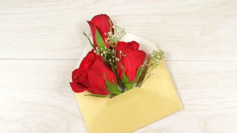 Opened-yellow-envelope-with-red-roses-on-white-wooden-background-4k