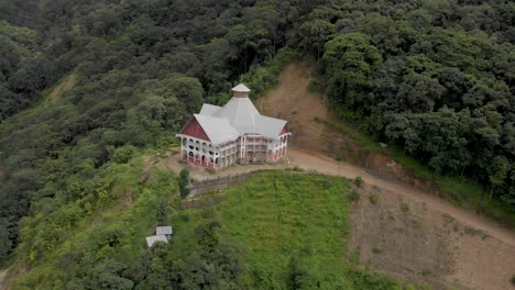 4k-Aerial-Right-to-Left-Spiral-shot-of-Khonoma-Cathedral-built-in-Naga-Architecture-covered-in-Fog,-Nagaland,-India