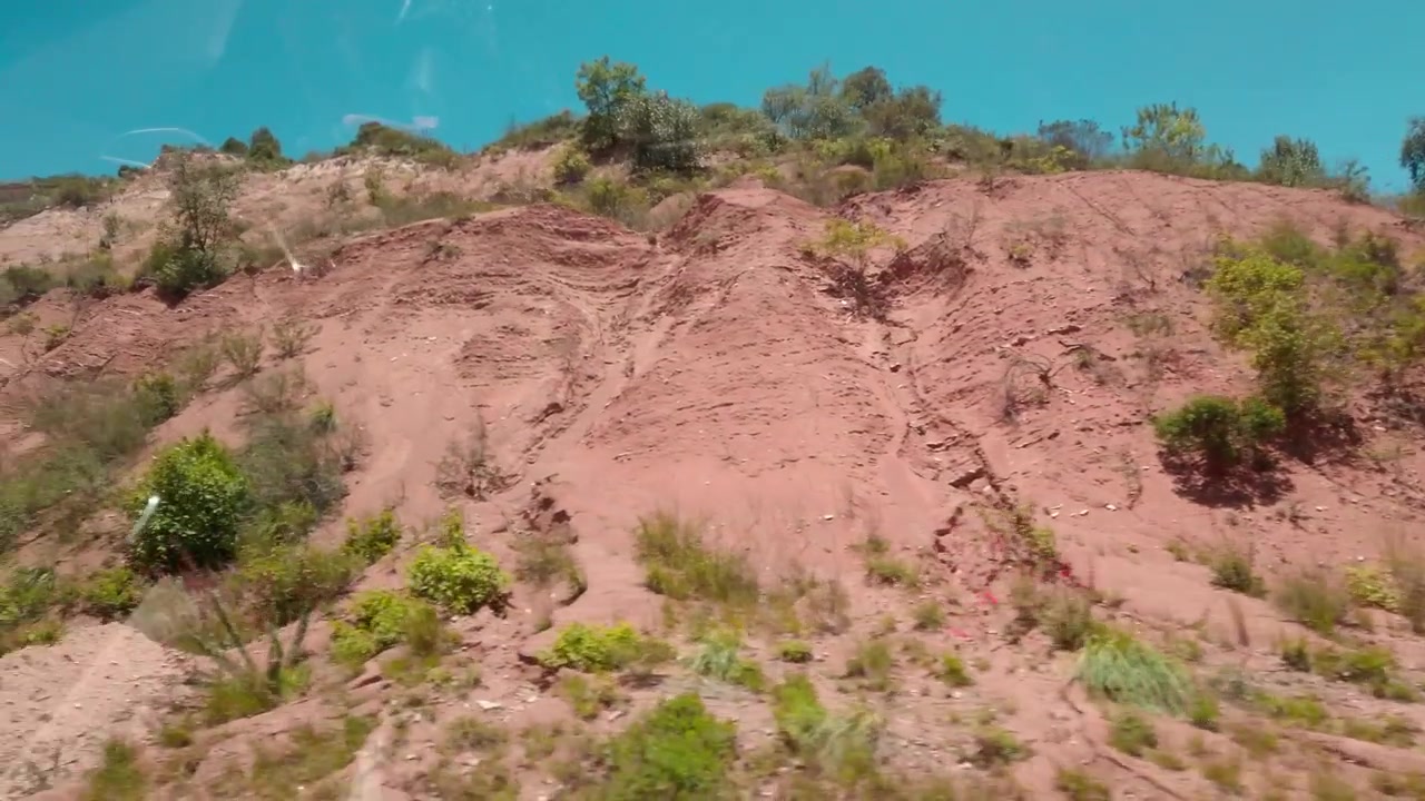 Vista dall'auto che attraversa una collina rocciosa con arbusti di terreno arido e vegetazione stradale vicino a Huatulco, Oaxaca, Messico, sotto un cielo azzurro e limpido di giorno