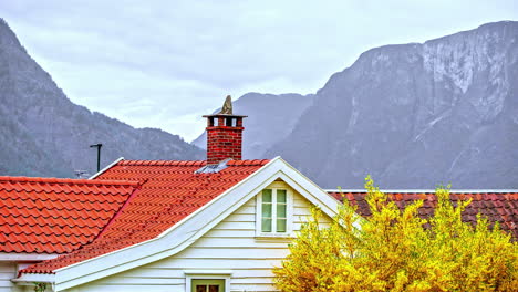 a house in the foreground with rugged mountains and cliffs in the background at daytime with an overcast sky - time lapse