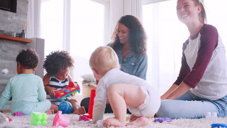 two women talking and playing with toddlers on the floor