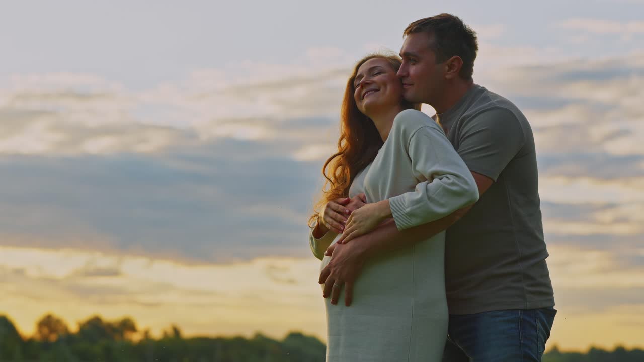 A pregnant couple embracing at sunset