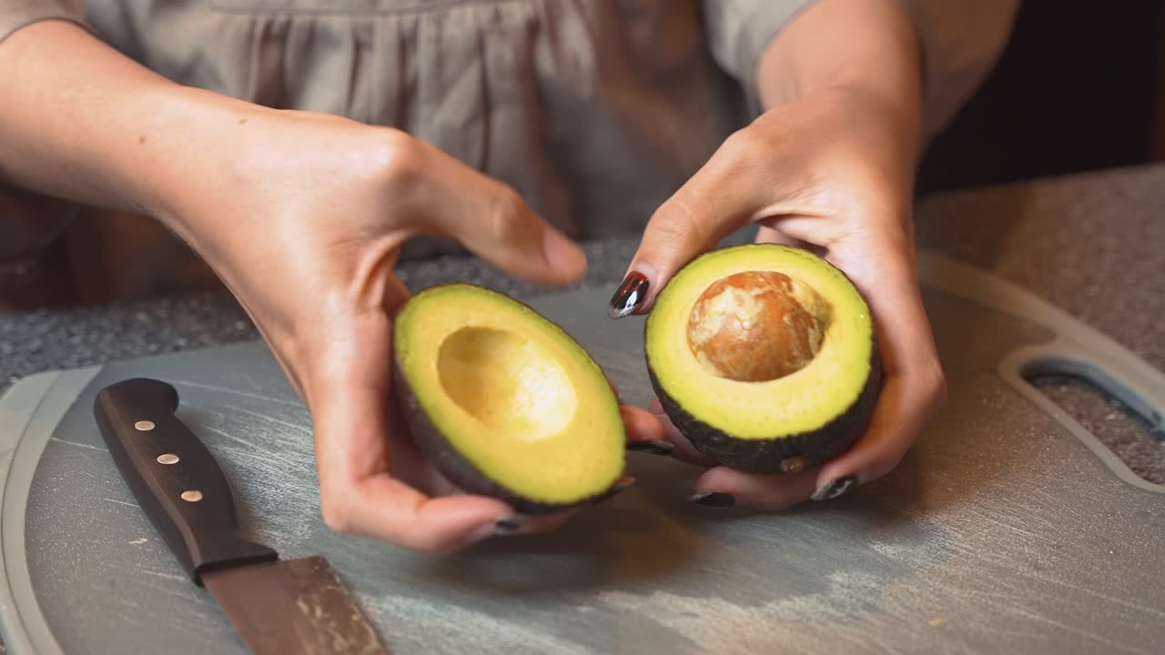 Woman's hands cutting open avocado on chopping board with knife, close up shot