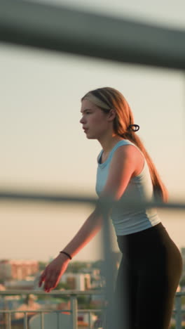 young lady roller skating outdoors, with focus on iron railing in foreground, cityscape with buildings and sunset glow is visible in blurred background