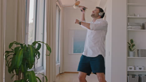 happy travel man dancing in hotel room having fun listening to music celebrating summer vacation enjoying carefree holiday lifestyle wearing headphones