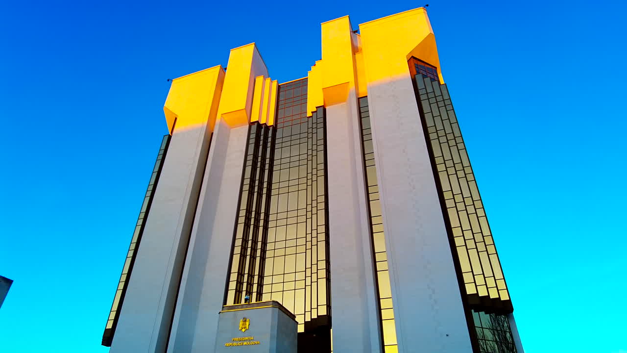 Under bright blue skies, a stunning building with a bold yellow roof reflects sunlight. It showcases modern architecture in a lively urban environment, captivating passersby