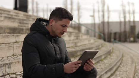 Side-view-of-young-man-with-ear-tunnels-watching-video-online-outdoor