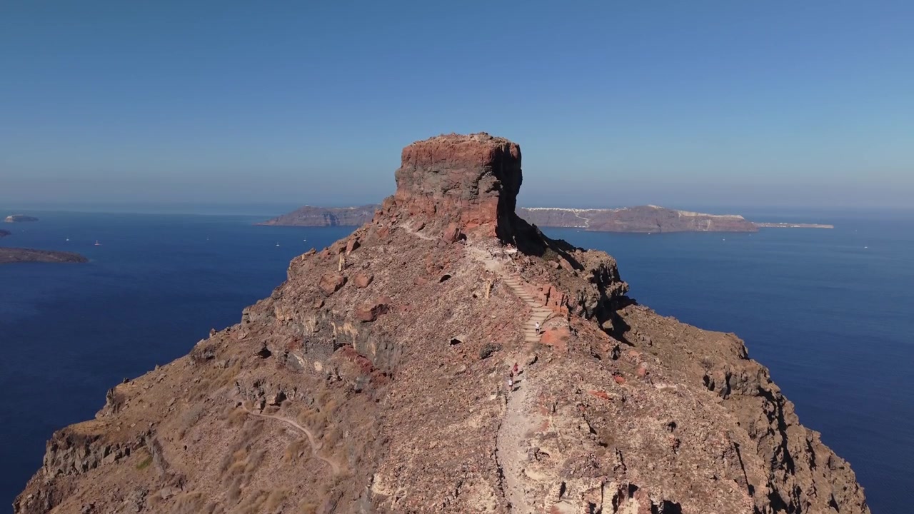 Drone che sale sopra Skaros Rock a Santorini, catturando le spettacolari scogliere vulcaniche e il paesaggio unico della caldera sopra il profondo Mar Egeo.