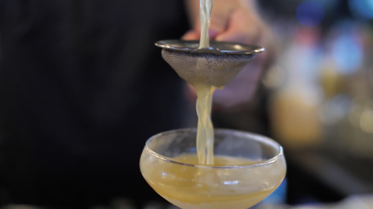 Profesjonell bartender heller fruktcocktail i glass gjennom sil, nærbilde