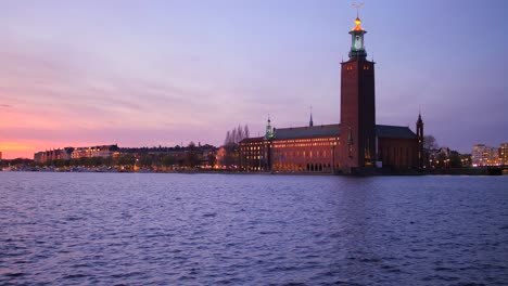 view of stockholm city hall from gamla stan across riddarfjarden in stockholm, sweden at sunset