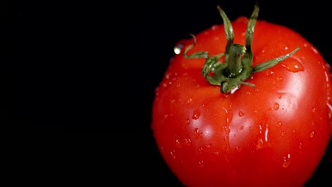 un tomate fresco cayendo gotas de agua.