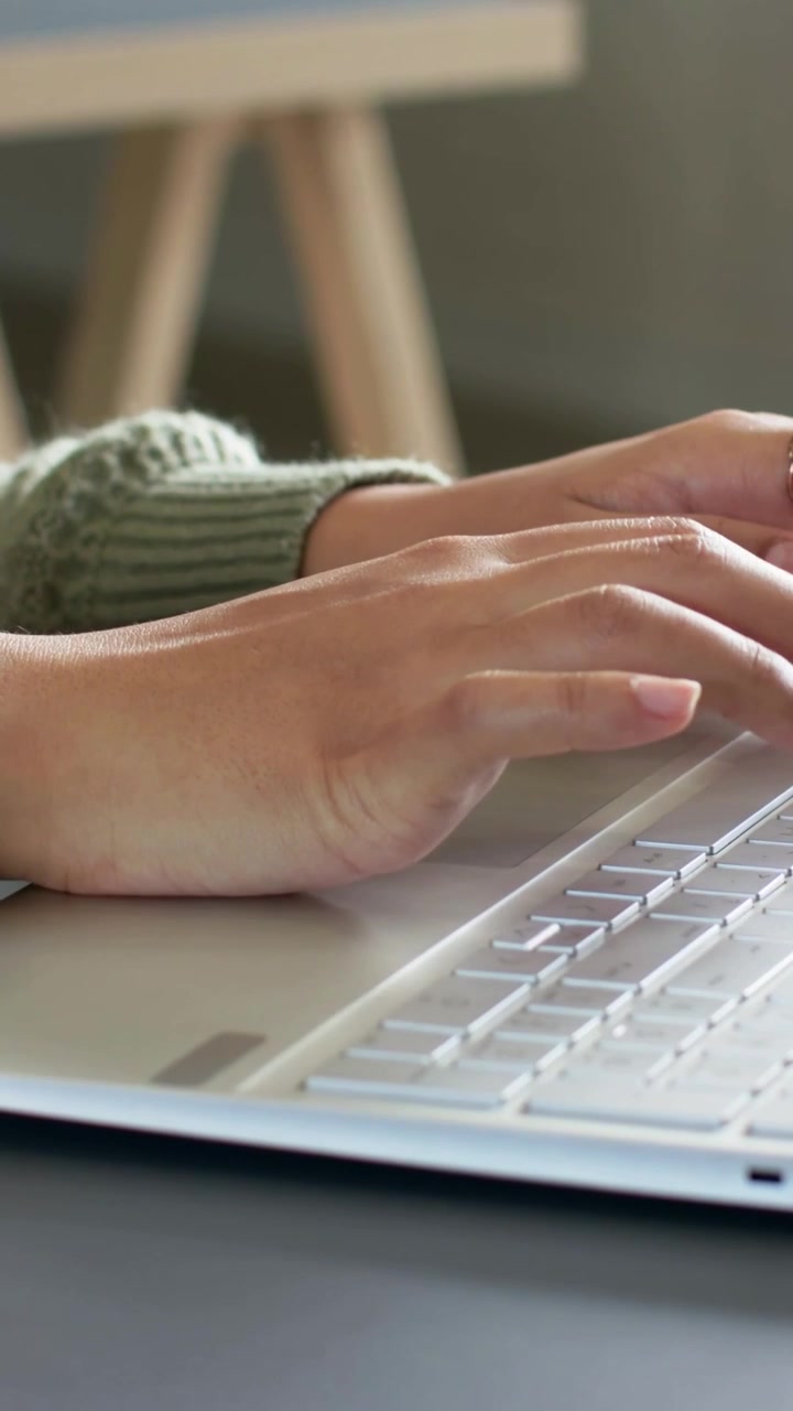 Typing woman's hands in green sweater on white laptop keyboard at home, showing smartwatch and ring