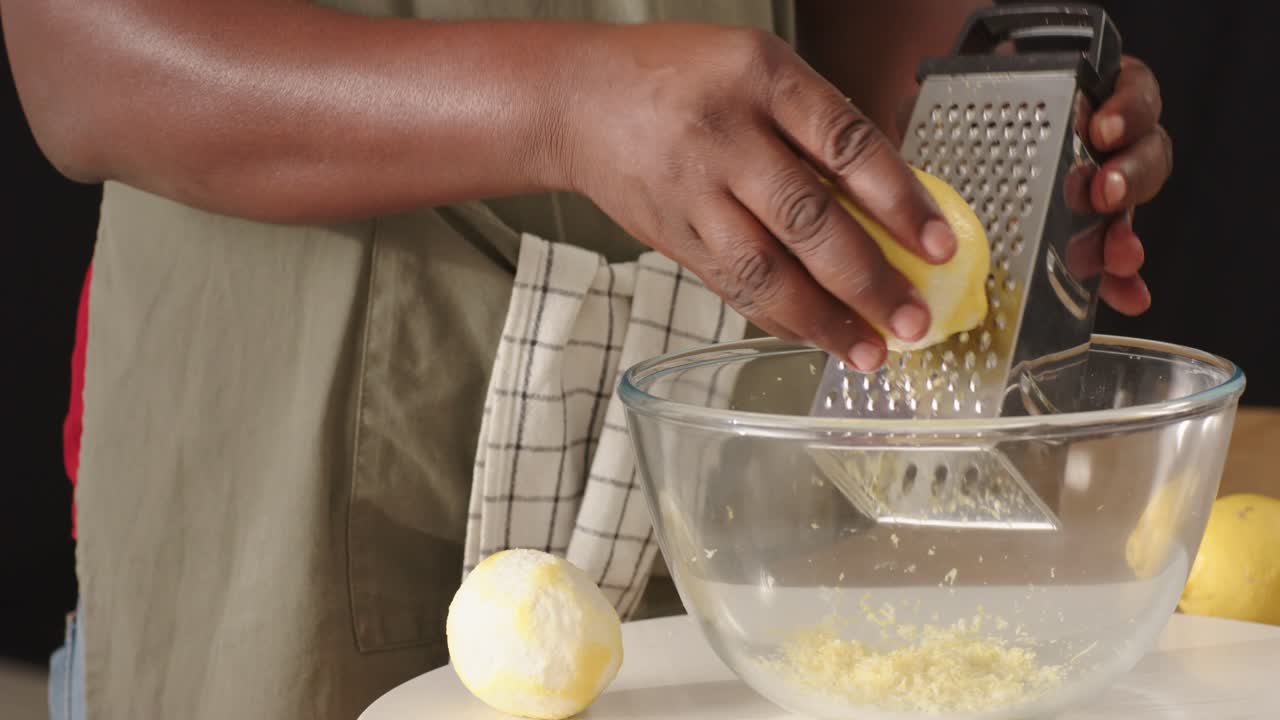 Uomo di mezza età che tiene un limone tagliato a metà, grattugiando la scorza con una grattugia a quattro facce in una ciotola di vetro in cucina per insaporire.