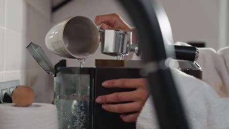 woman pours water into coffeemaker tank in kitchen closeup. lady fills water tank using cup preparing hot drink in morning. servicing coffee machine