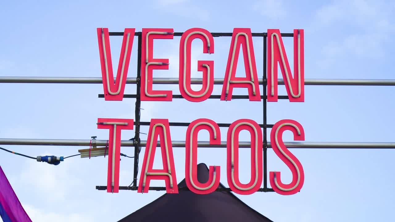 signo de neón masivo por encima de la tienda en color rojo bombilla de línea interior conectada a una fuente eléctrica principal de cable para alimentar la señal planta basada en comer tienda lgbtq+ bandera en el lado cielo despejado con pocas nubes