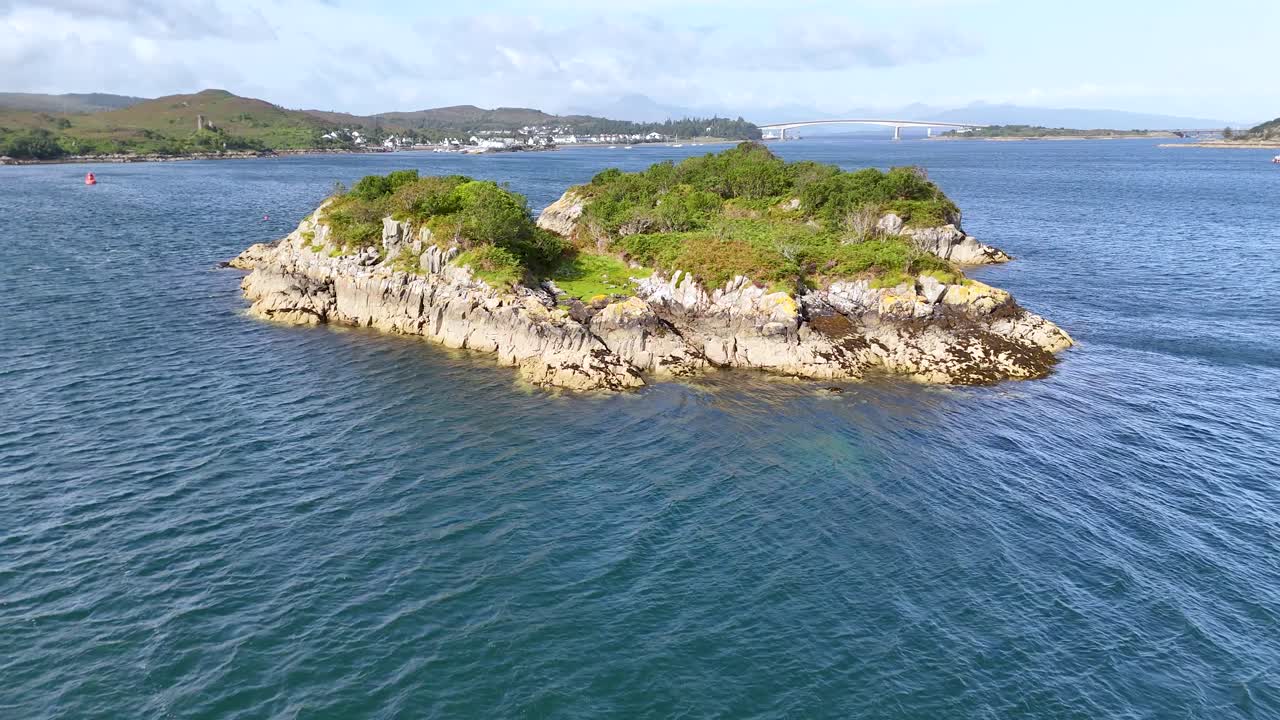 Drone circles lush, rocky island in blue sea near Scotland’s Isle of Skye
