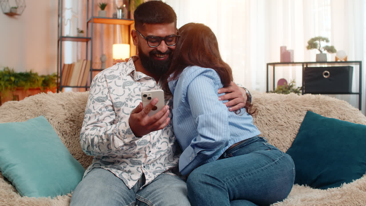 Indian family couple man woman celebrating lottery win on smartphone surprised excited by jackpot