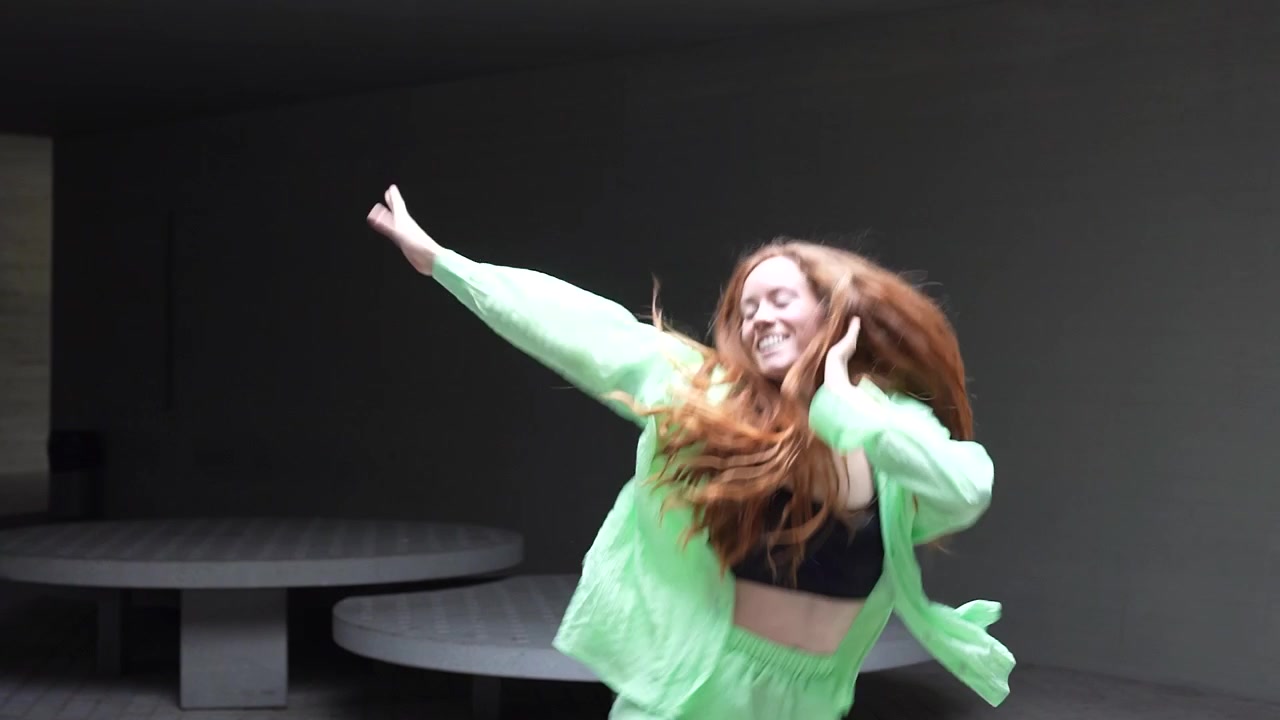 A vibrant and youthful woman wearing a neon green outfit dances with joy in a modern setting