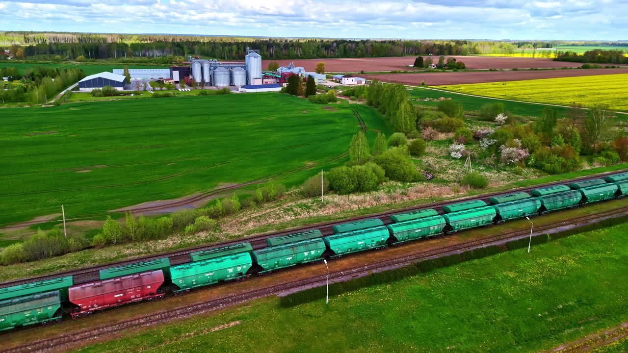 Train passing through lush fields, industrial site in the background