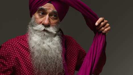 low key studio lighting shot of senior sikh man with beard tying fabric for turban against dark background 2