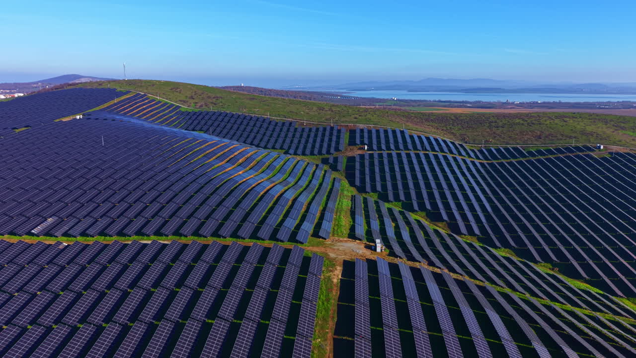 Rækker af skinnende solpaneler dækker de bølgende bakker under en lys blå himmel en solrig morgen, hvilket viser vedvarende energi i aktion.