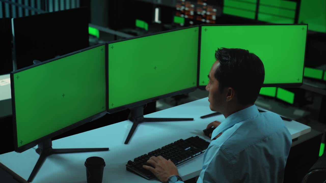 vista lateral de un hombre asiático trabajando con múltiples monitores de computadora en la oficina