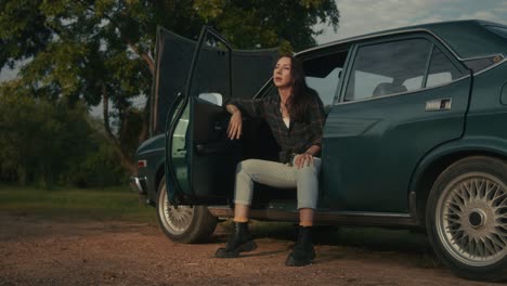woman sitting on a vintage green car by the roadside