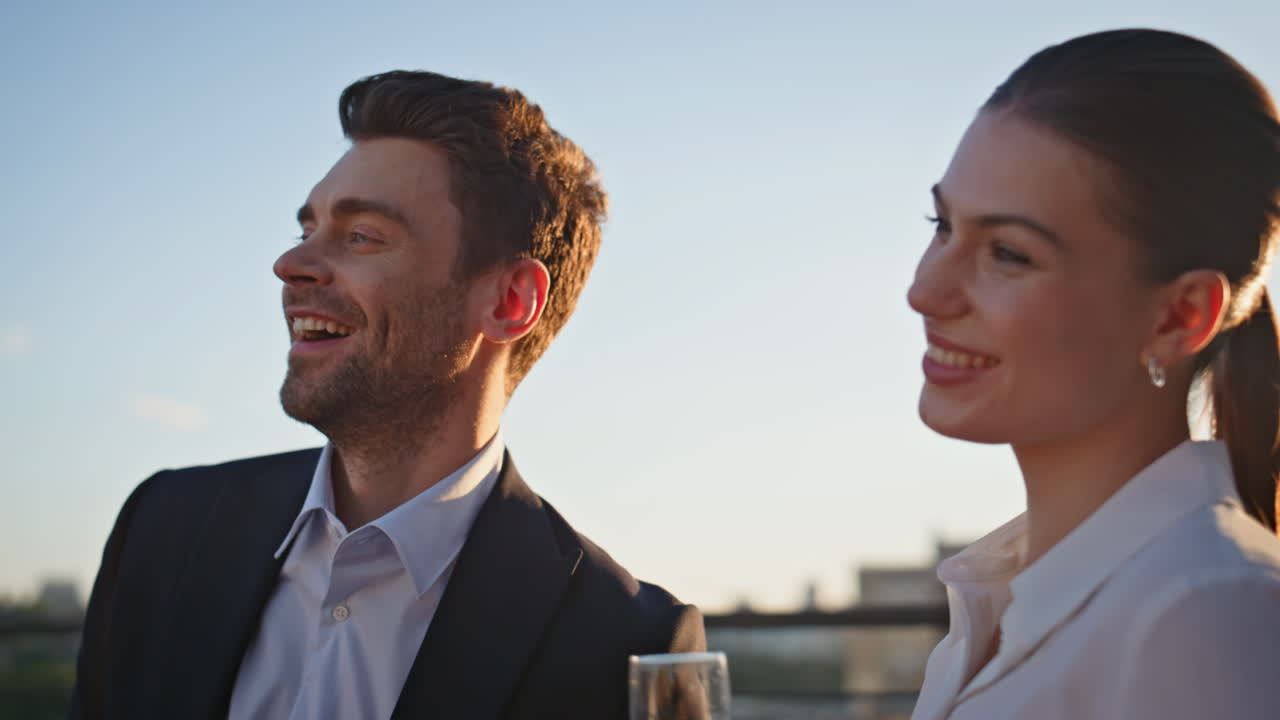 Smiling couple clinking champagne glasses at sunset rooftop party closeup
