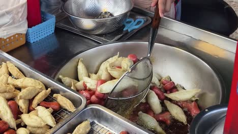 street food vendor preparing fried fish cakes and sausages