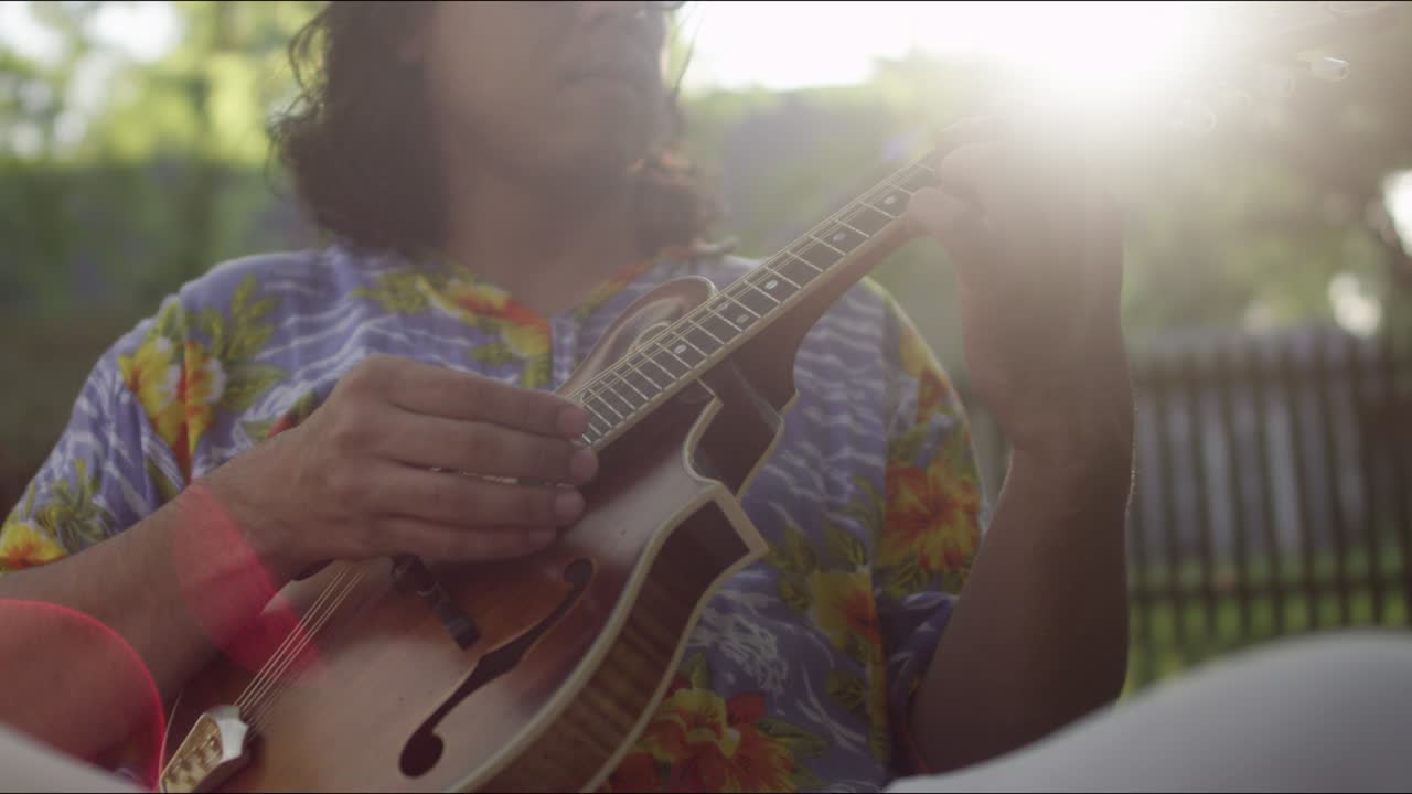 A young man plays a small guitar for friends at a summer barbecue