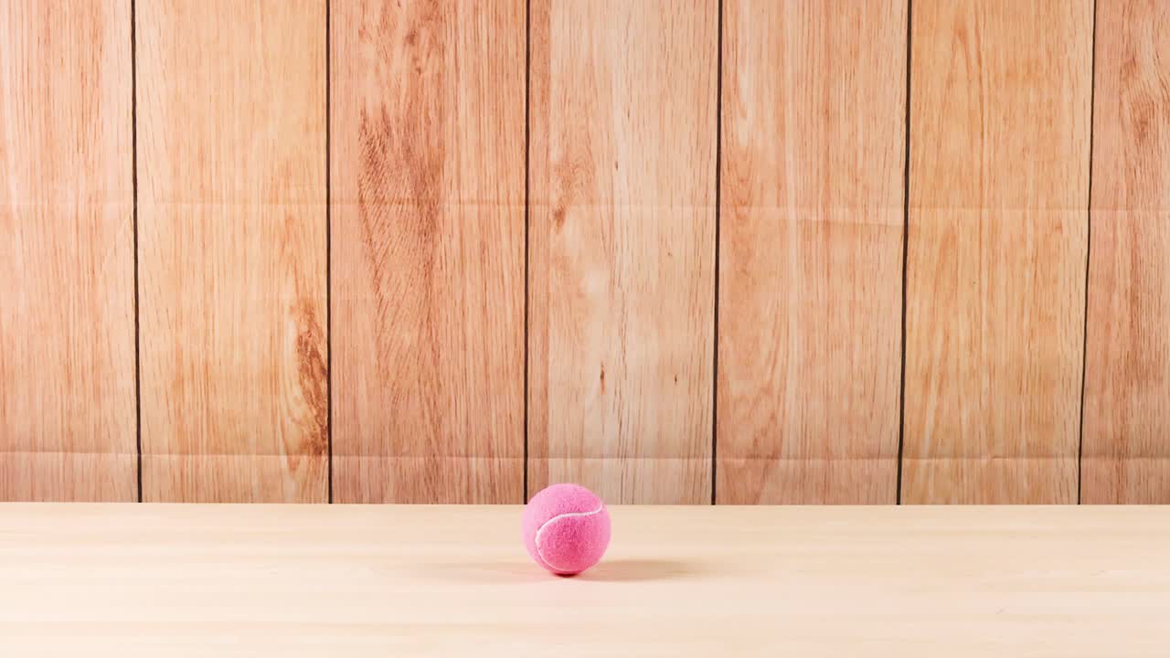 Pink ball bounces against wooden background repeatedly