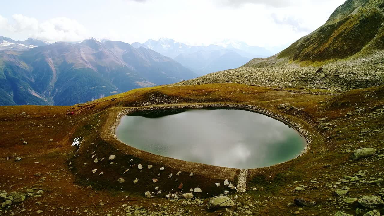 Rocky path leads to serene alpine lake surrounded by Swiss mountain peaks