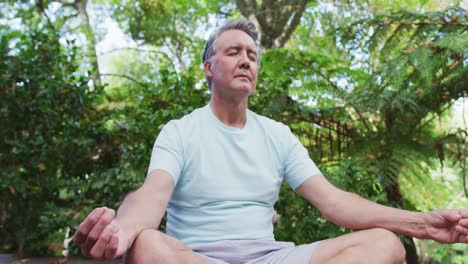 relaxed senior caucasian man practicing yoga sitting in lotus position meditating in garden