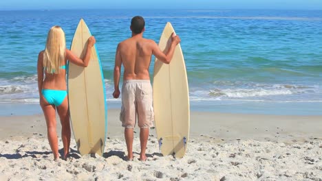 Couple-looking-at-the-sea-holding-their-surfboards