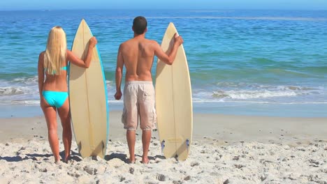 couple looking at the sea holding their surfboards