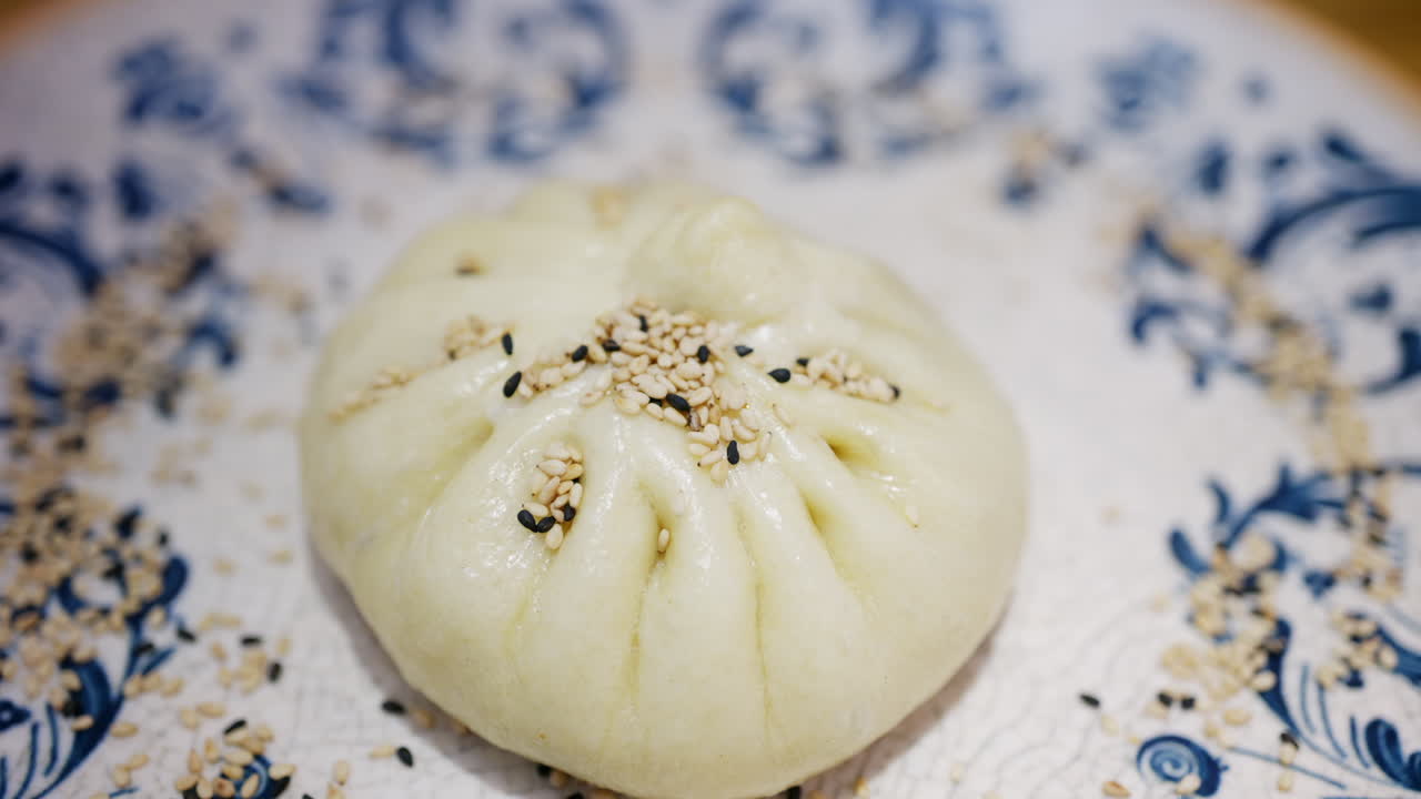 Cận cảnh một chiếc bánh bao hấp rắc hạt mè trên đĩa gốm trang trí.