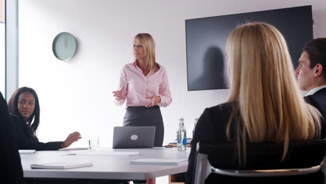 Mature-Businesswoman-Addressing-Group-Meeting-Around-Table-At-Graduate-Recruitment-Assessment-Day