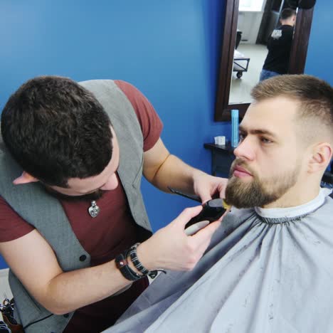 peluquero dando forma y recortando la barba del cliente usando cortapelos
