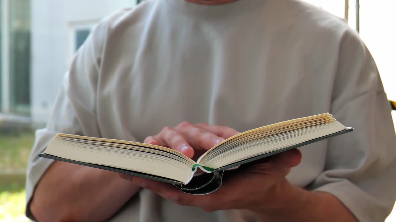 Man holding and reading a book turning pages slowly. Cropped footage